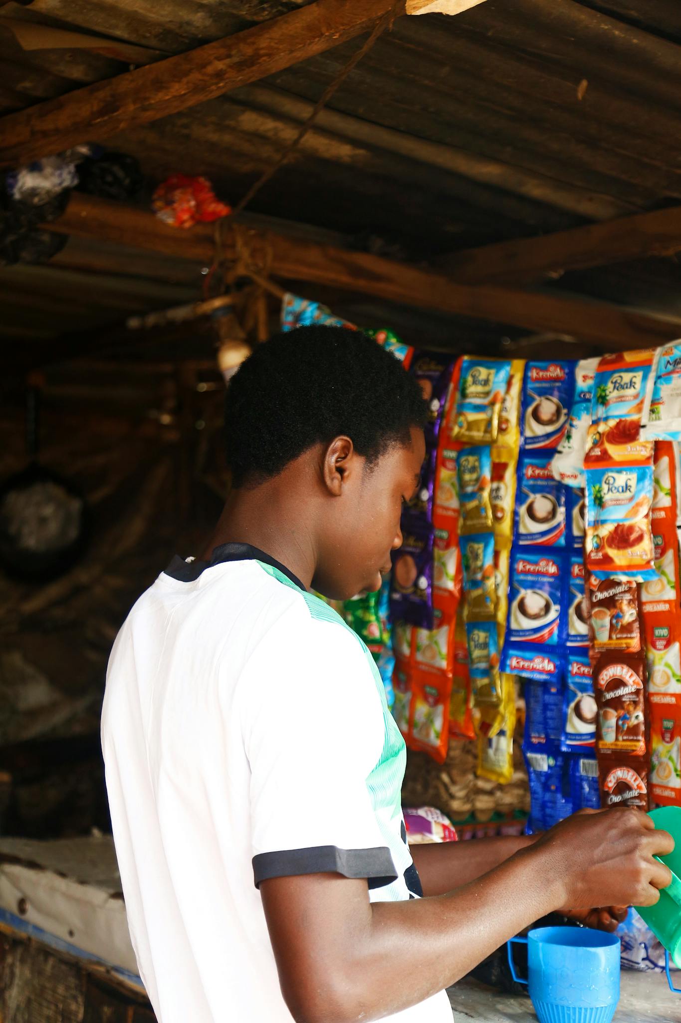 A vendor at an outdoor market in Abuja, Nigeria prepares a beverage amidst colorful product packaging.